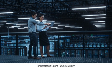 Data Center Female System Administrator and Male IT Specialist Talk, Use Laptop Computer. Information Technology Engineers work on Cyber Security Network Protection in Cloud Computing Server Farm. - Powered by Shutterstock