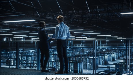Data Center Male IT Specialist and Female e-Business Enrepreneur Talk, Use Laptop. Two Information Technology Professionals on Bridge Overlooking Cloud Computing Server Farm. - Shutterstock ID 2030685752