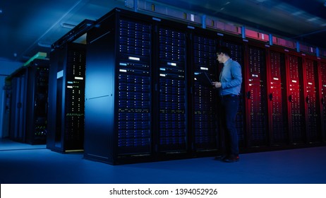 In Data Center: Male IT Specialist Walks along the Row of Operational Server Racks, Uses Laptop for Maintenance. Concept for Telecommunications, Cloud Computing, Artificial Intelligence, Supercomputer