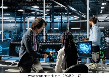 Data center manager teaching intern how to run AI forecasting simulations, tracking performance. Server hub supervisor helping trainee learn to integrate machine learning APIs into software platforms