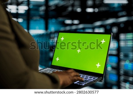 Data center programmer uses a green screen laptop in a data center for equipment maintenance, screen replacement, and server workflow monitoring.