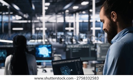 Data center programmer using laptop to monitor neural network using AI LLM chatbot. Worker using artificial intelligence on notebook to oversee servers powering machine learning, camera A