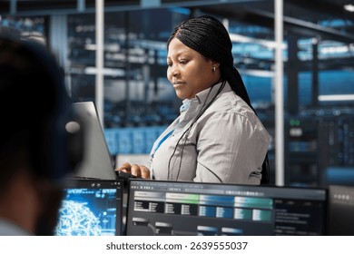 Data center software developer using artificial intelligence neural networks tech. African american server farm employee using AI programming language on computer, configuring specialized hardware