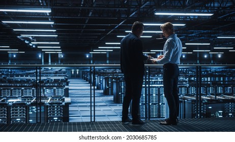 Data Center IT Specialist and e-Business Enrepreneur Talk, Use Laptop. Two Information Technology Professionals Walking on Bridge Overlooking Cloud Computing Server Farm.