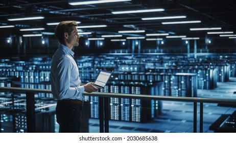 Data Center Specialist Engineer Using Laptop Computer. Server Farm Cloud Computing Facility with Male System Administrator Working. Data Protection Network for Cyber Security.