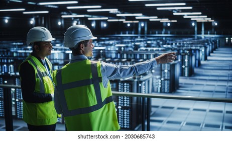 Data Center IT Specialist and System administrator Talk, Use Tablet Computer, Wearing Safety Wests. Server Clod Farm with Two Information Technology Engineers checking Cyber Security. - Powered by Shutterstock