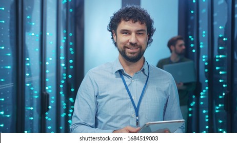 Data Center Specialist Working On Digital Tablet In High Tech Server Room. Handsome Cheerful Technician Smiling At Camera Coworking In Computer Security.