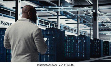 Data center system administrator checking infrastructure diagnostics using tablet screen. IT specialist walking in high tech server room, examining data charts during system audit, camera A