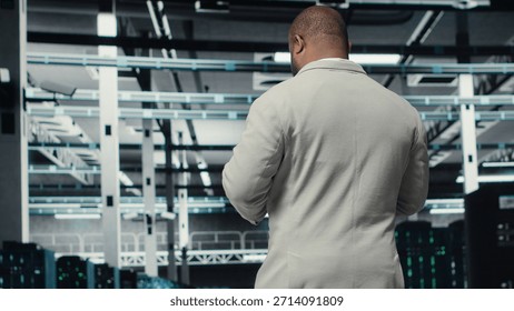 Data center system administrator checking infrastructure diagnostics using tablet screen. IT specialist walking in high tech server room, examining data charts during system audit, camera B