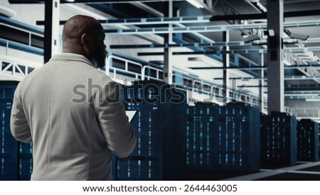 Data center system administrator checking infrastructure diagnostics using tablet screen. IT specialist walking in high tech server room, examining data charts during system audit, camera A