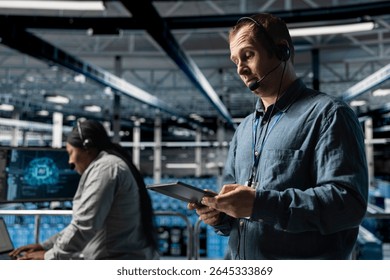 Data center system administrator using headset mic, providing remote diagnostics using tablet. Server room worker monitors system health and guides users through infrastructure troubleshooting steps