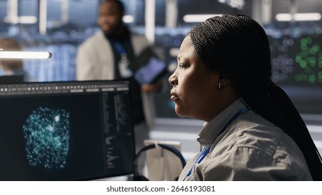 Data center system administrator using PC to monitor neural network AI visualization. African american woman in server room using computer to oversee rigs powering machine learning processes, camera A