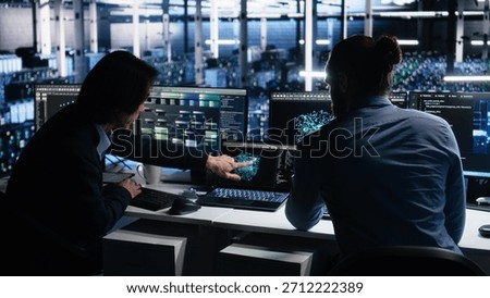 Data center system administrators use PC to monitor neural network using AI LLM. Asian man and colleague at work using artificial intelligence to oversee servers powering machine learning, camera A