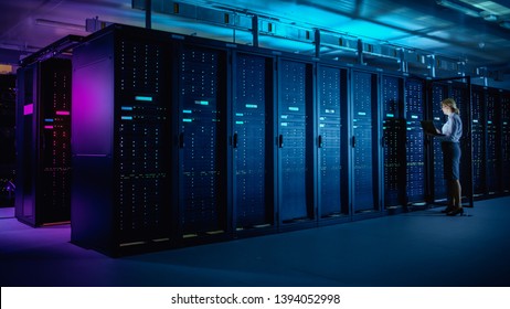 In Data Center: IT Technician Running Maintenance Programme on Laptop, Controls Operational Server Rack Optimal Functioning. Modern High-Tech Telecommunications Operational Data Center in Neon Lights.