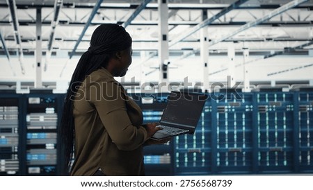 Data center worker using laptop to manage software updates for system stability. African american woman in server room configuring infrastructure for optimum performance, camera B