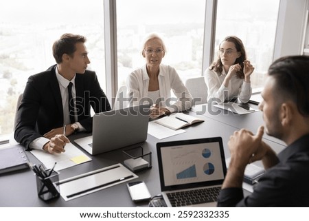 Data driven discussion. Diverse age business team professional managers executives work talk negotiate at conference desk brainstorm solution strategy based on statistic information on notebook screen