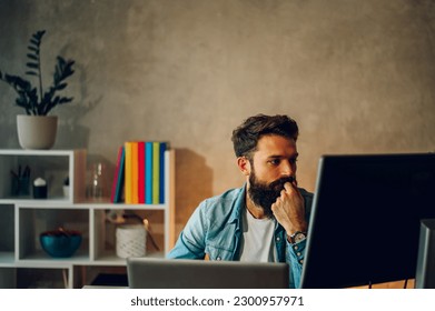 A data entry expert is looking at a database on his monitors in a cozy home office at night. A data analyst is working from a home office at night while looking at the database on his two screens.