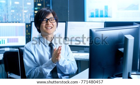 In the Data Mining Center Statistician Claps His Hands while Sitting at His Workstation Surrounded with Monitors Displaying Data and Graphs.