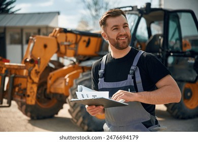 Data in the notepad, reading. Man is with tractor. Agricultural worker.