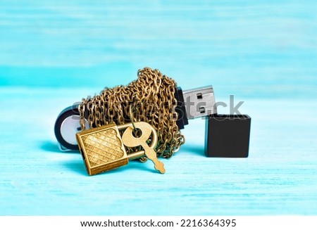 Data security concept: flash drive wrapped in chains and secured with a tiny padlock on a blue wooden background.