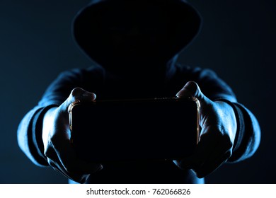  Data theft or cyber security concept. Hacker holding a smartphone with a blank screen in a cool tone.