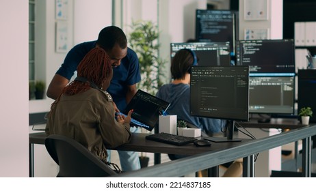 Database developer explaining algorithm to colleague coder pointing at running code on laptop. System engineers collaborating on development group project, using terminal window.