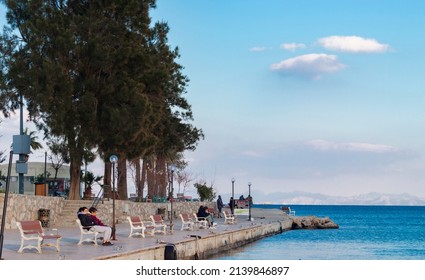 Datca, 03.03.2022 : Coastal Area Of Datça Peninsula In Turkey. People Sitting On Bench And Watcin Blue Sea View. Quiet, Peaceful Seaside Town.	
