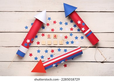 Date 4 JULY with firework rockets and stars on white wooden background
