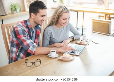 Date in cafe. Young couple in cafe with stylish interior. Students having delicious coffee drinks. They chatting, using laptop and smiling - Powered by Shutterstock