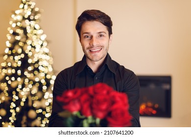 Date Concept. Portrait Of Happy Bearded Young Guy In Black Shirt Holding Bunch Of Fresh Flowers And Giving Bouquet Of Red Roses To Camera. Celebrating Holiday, Anniversary, Valentine's Day, 8 March