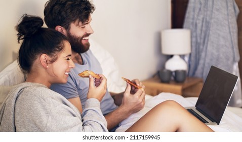 Date night done right. Shot of a happy young couple using a laptop and eating pizza while relaxing on the bed at home. - Powered by Shutterstock