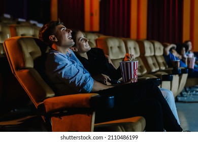 Date at night at the movies!. Portrait of happy young couple sitting in cinema auditorium eating popcorn and watching comedy movie together. Entertainment and togetherness concept - Powered by Shutterstock