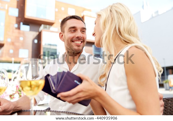 date, people,\
payment and finances concept - happy couple with wallet and wine\
glasses paying bill at\
restaurant