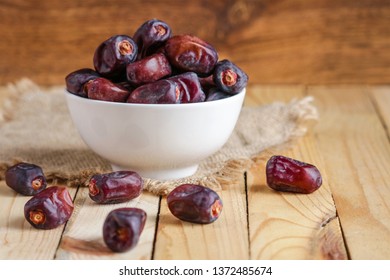 Dates Fruit  In White Bowl And Scattered On Wooden Table  