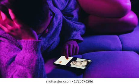 Dating app or site in mobile phone screen. Woman lies on sofa swiping and liking profiles on relationship site or application. Single woman using smartphone to find love, partner and girlfriend.