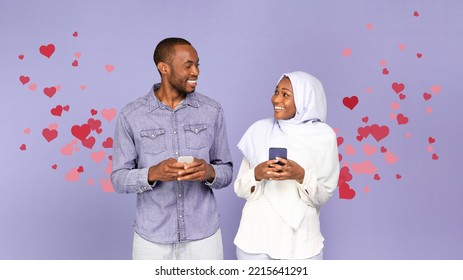 Dating Application. Happy Muslim Black Couple Texting On Smartphones Smiling To Each Other Standing Over Purple Studio Background With Hearts Icons. Panorama, Collage