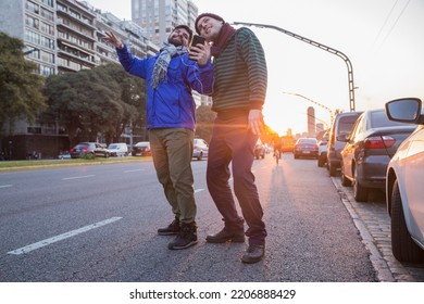 A Dating Happy Gay Couple Listening Music From Mobile By Sharing Headphones While Dancing In The Middle Of The Street At Golden Hour. LGBTQ People Life. Copy Space.		