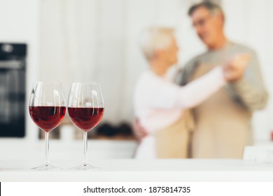 Dating In Older Age. Unrecognizable Senior Couple Dancing Having Romantic Date At Home, Focus On Two Glasses Of Wine. Spouses Dance In Kitchen Enjoying Weekend Indoor. Love Relationship In Retirement