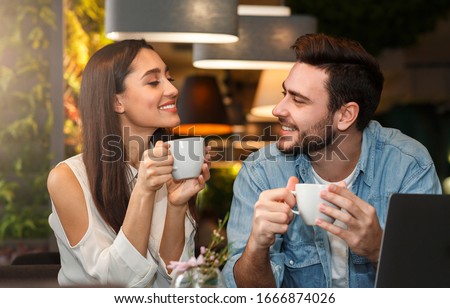 Dating. Young couple tasting coffee drinks enjoying flirt and conversation during weekend date sitting in cozy cafe
