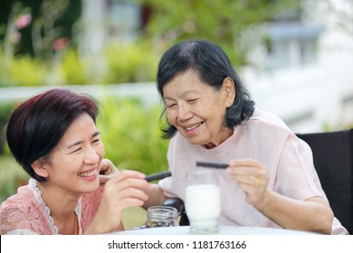 Daughter Caring For The Elderly Asian Woman ,picking A Chocolate Cookie To Mother In Backyard.