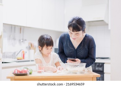 Daughter Cooking With Her Mum And Looking At A Recipe On Her Phone