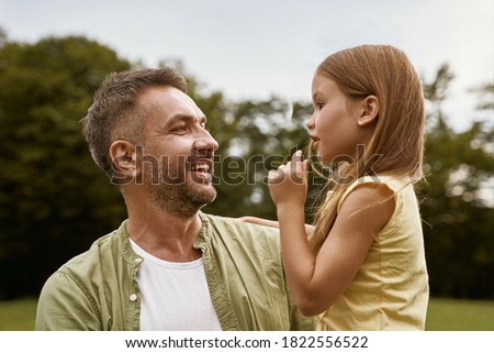 Daughter and daddy. Cute little girl spending time with father while visiting park on a summer day, they are talking and smiling