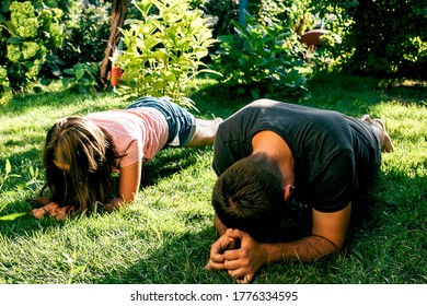 Daughter And Father Doing Planking Exercise On Grass In Garden. Family Sport Concept