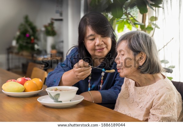Daughter feeding\
elderly mother with\
soup.