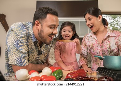 Daughter giving her father, in a wooden spoon, a sample of sauce that she has cooked with her mother.