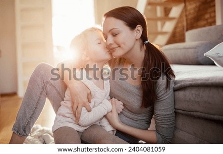 Daughter giving her mother a tender kiss on the cheek in a sunlit living room