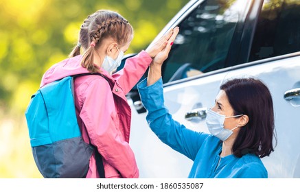 Daughter Giving High Five To Mother After School Standing In Protective Masks Near Car On Parking