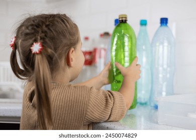 Daughter helps mother sort plastic in the kitchen at home. A child takes a plastic bottle to put it in a recycling box. Collecting and sorting plastic in the kitchen for recycling. - Powered by Shutterstock