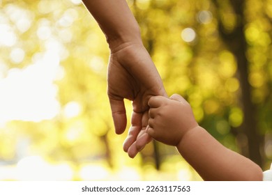 Daughter holding mother's hand outdoors, closeup. Happy family