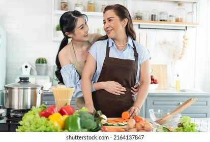 Daughter Hug And Kiss Mother. Asian Family Making Salad In Kitchen At Home Together.